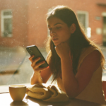 Une jeune femme consulte son smartphone en terrasse de café, illustration de la recherche visuelle Instagram