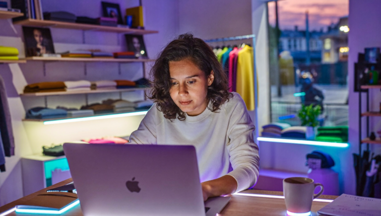 Commerçante qui prépare ses prix du Black Friday dans Shopify Rollouts sur un ordinateur portable, derrière le comptoir de sa boutique